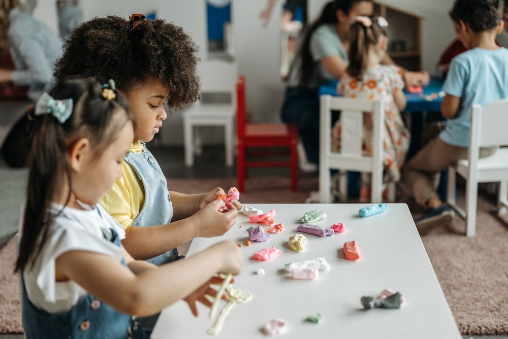 Preschool children shaping colorful clay together at a classroom table