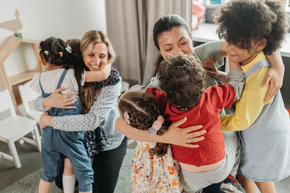 Daycare teachers and children sharing a group hug indoors